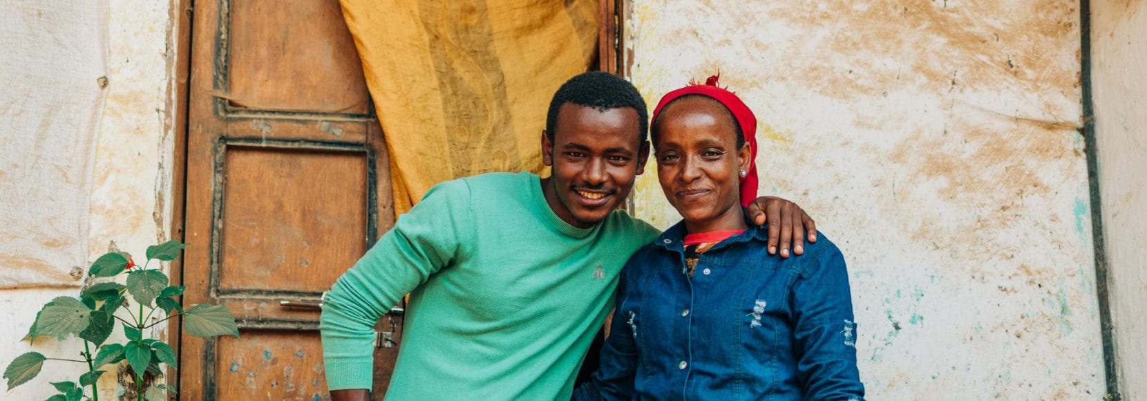 The impact of coffee has transformed what life looks like for Lubaba and her son smiling in front of their home