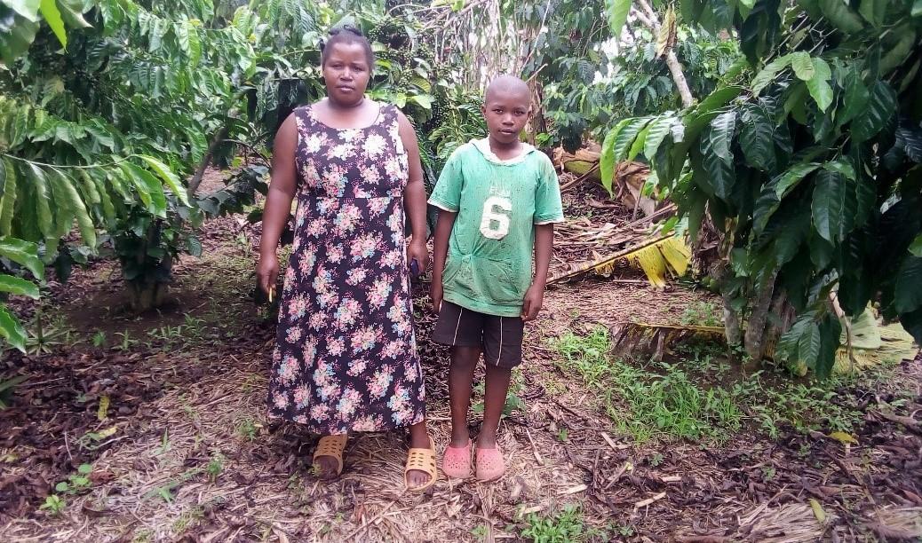 Coffee farmer Ovia Biringwa stands with her son on their farm in Uganda