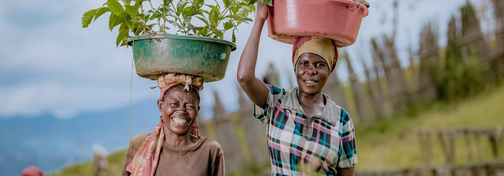 TechnoServe 2023 Annual Report Cover image of two women smiling in Rwanda carrying containers with green plants in them on their heads.