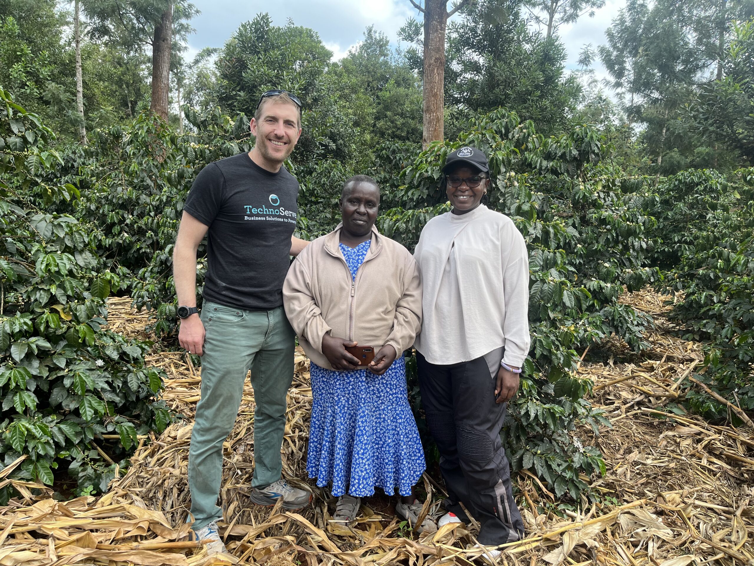 TechnoServe Country Director Kris Ansin stands with two women in a coffee field in Kenya. Part of a blog post highlighting the Kenyan president's state visit. 