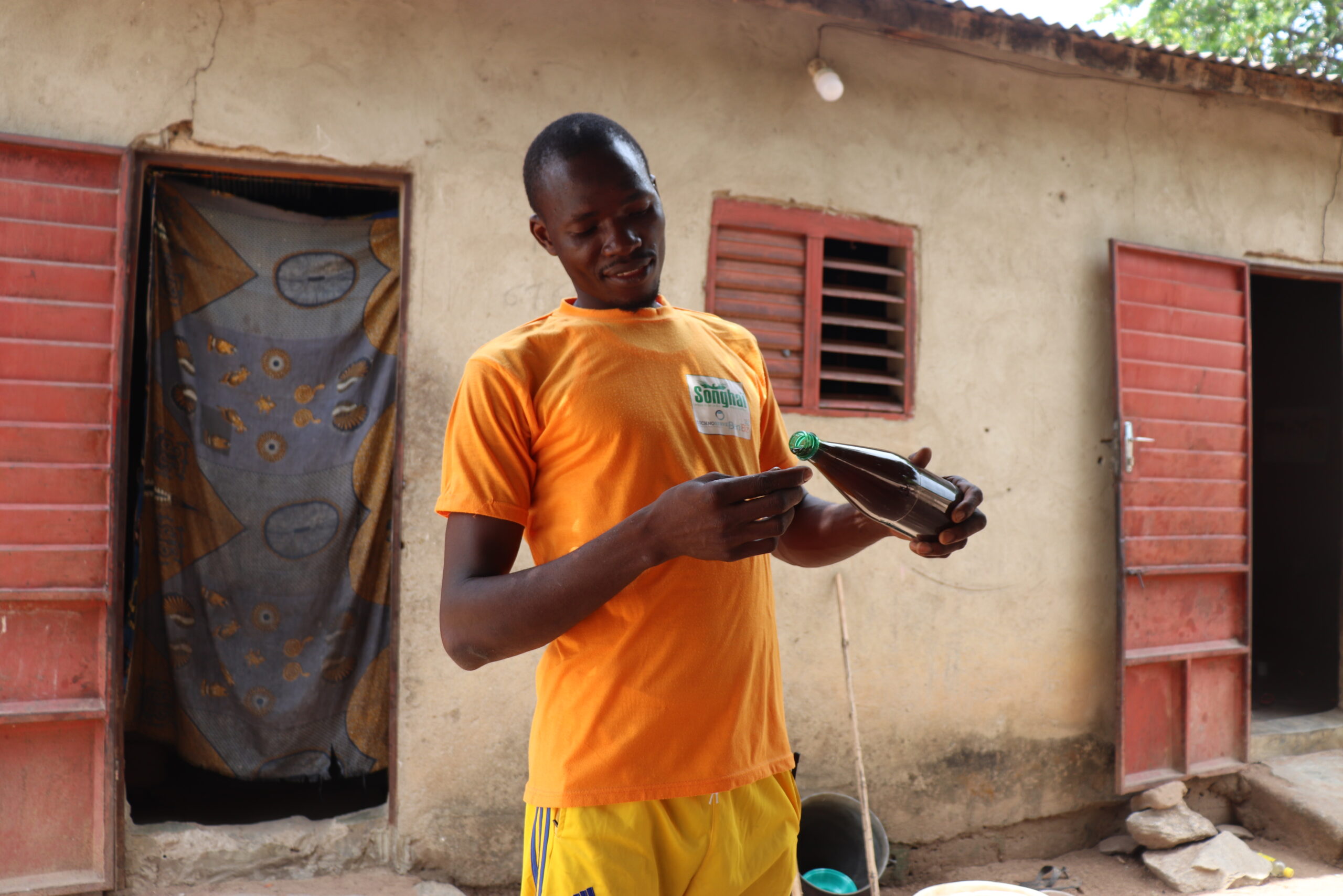 Baranon, in an orange shirt, pours a sample of honey from a bottle while standing in front of his home, highlighting his beekeeping work. (TechnoServe) 