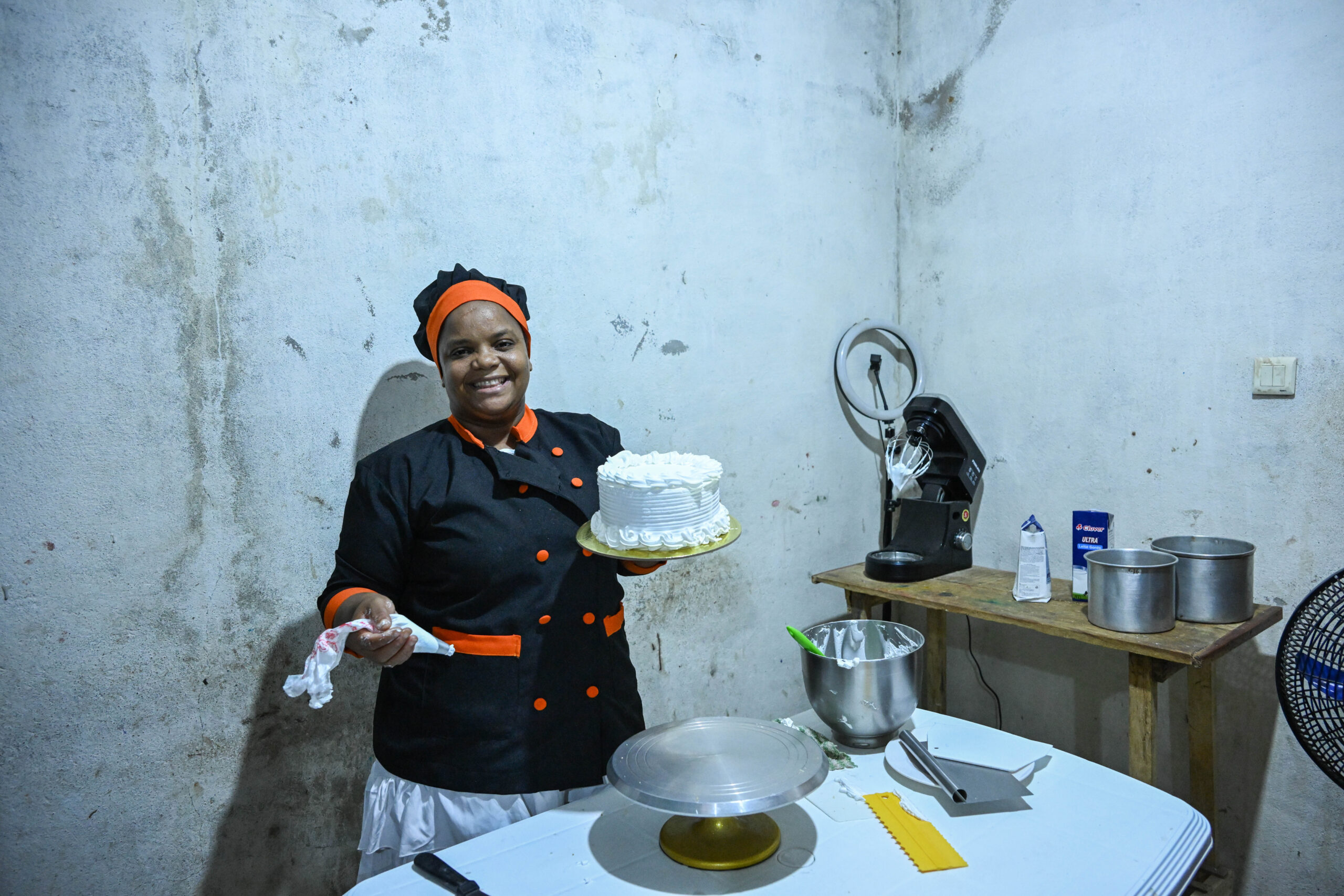 Baker and Teacher Lucia Sigauque smiling as she decorates a cake in her bakery. Lucia's growing business is creating new jobs and teaching other women the skills they need to open their own baking businesses, creating a ripple effect for the women she impacts in her community.