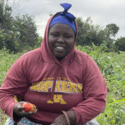 A woman kneels in a field with a bucket of tomatoes.