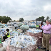 A man in a pink shirt takes a photo of a recycling center in Nigeria.