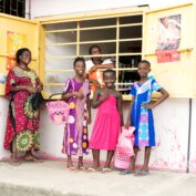 Women and children smile outside a micro-retail shop in Nigeria.