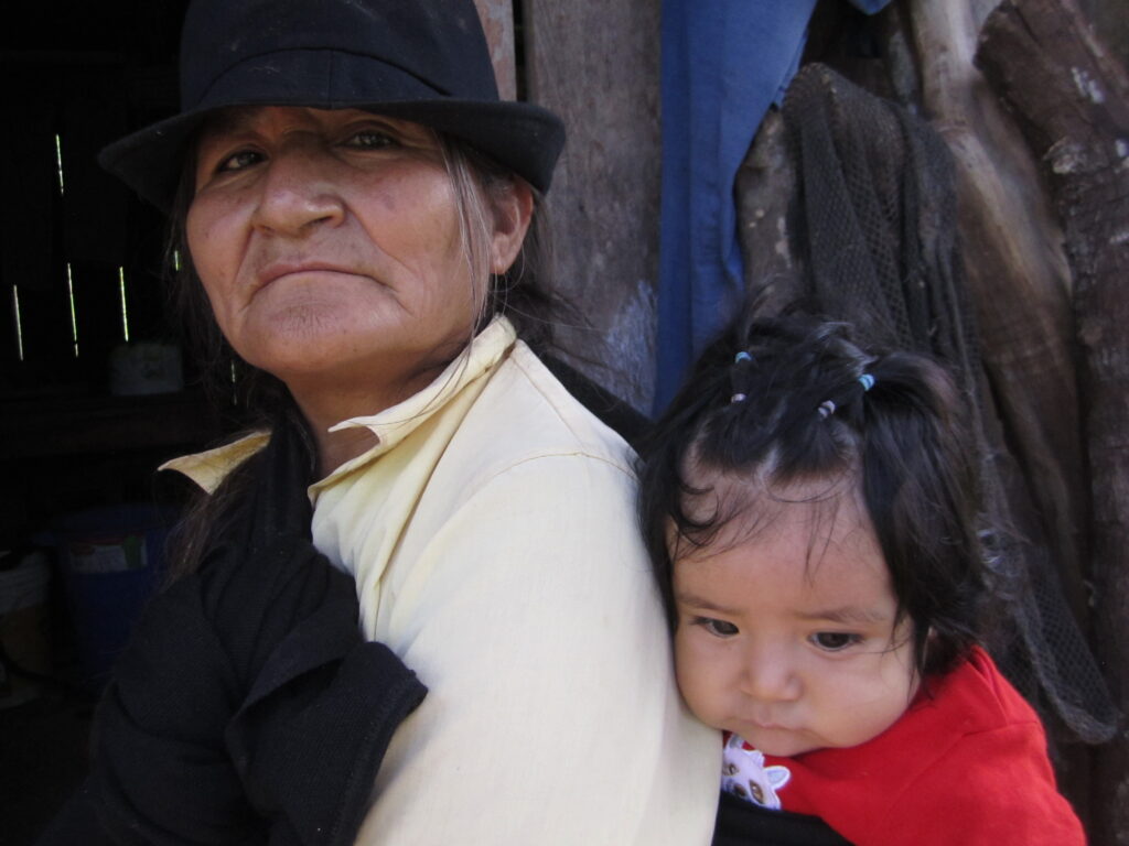 Woman carrying a baby on her back, symbolizing love and family connection in a rural setting.